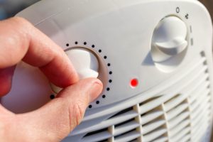 Man's hand adjusts the temperature of the electric fan heater at
